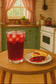 Glass of cherry tea with ice and a slice of cherry pie on a wooden table in a kitchen.