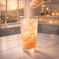 Dreamsicle orange cream loaded tea powder being poured into iced drink in cozy magical kitchen setting
